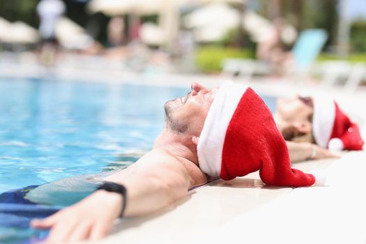 Young people in santa claus hats lie relaxed in pool. Tourism vacation for New Year holidays concept