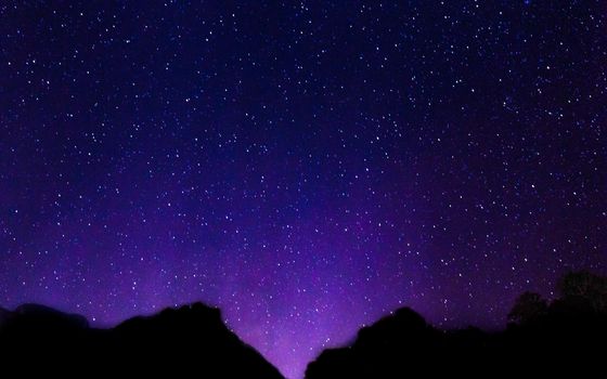 Night sky with lot of shiny stars with blurred mountain background .