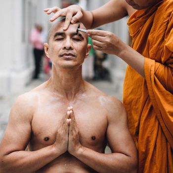 Close-up image of a handsome asian man is shaving hair by head of man who is ordained in Buddhism