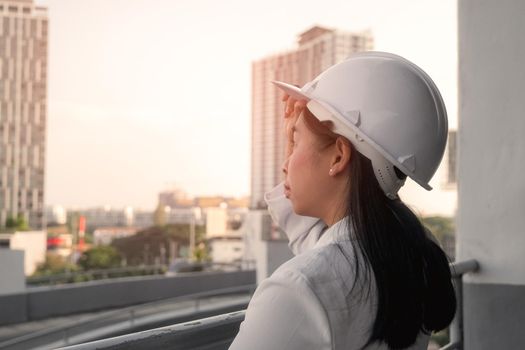 Female construction engineer with a tablet computer at a construction site. Confident woman architect in white helmet looking at a construction site. Construction and architecture concept.