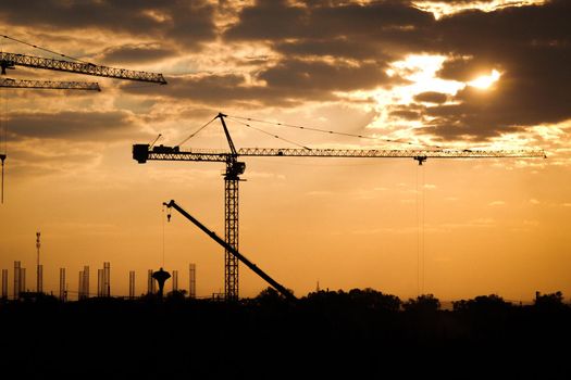 Silhouette of tower crane and large buildings construction site at sunset in evening time. New construction site with cranes on sunset background.