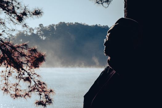 Asian senior man enjoying nature and warm morning sun in winter pine forest. Elderly man relaxing in the park . Outdoor leisure lifestyle of the elderly.