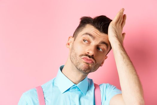 Close-up of handsome caucasian guy with moustache, feeling confident, touching his haircut and looking aside with smug face, standing on pink background.