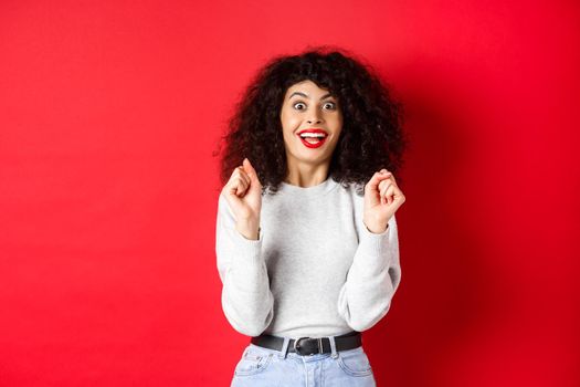 Excited woman winning prize, rejoicing and looking happy, smiling amazed, standing against red background.