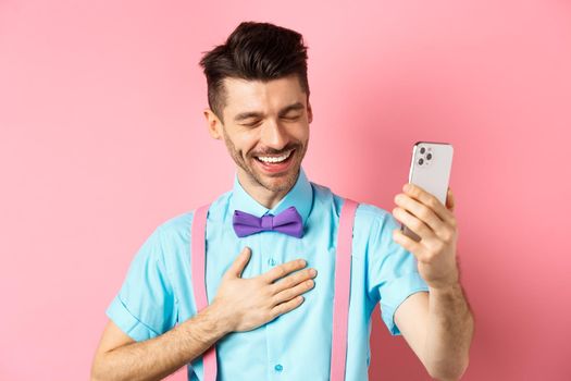 Image of handsome guy laughing during video chat, having mobile conversation and chuckle from something funny, standing on pink background.