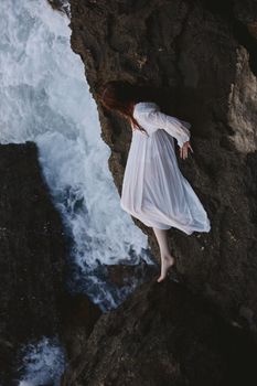 woman in long white dress wet hair lying on a rocky cliff Summer vacation concept. High quality photo