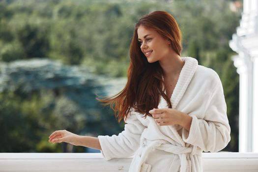 pretty woman with long hair in a white bathrobe staying on the balcony in a hotel unaltered. High quality photo