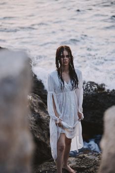 Woman in white dress with wet hair near the ocean with stones unaltered. High quality photo