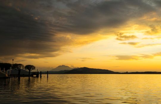 View of Lake Zugersee in the Swiss town of Zug at sunset with beautiful golden tones in the sky and reflected in the water and clouds.