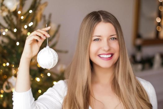 Christmas decoration and holiday mood concept. Happy smiling woman decorating xmas tree with festive toys and ornaments at home.