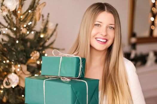 Christmas holiday and gifts for her concept. Happy smiling woman holding wrapped present boxes at home, xmas tree on background.
