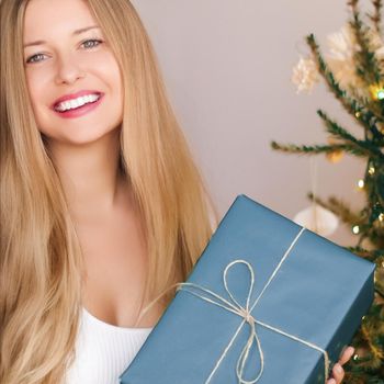 Christmas holiday and gift for her concept. Happy smiling woman holding wrapped present, xmas tree on background.