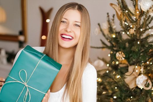 Christmas holiday and gift for her concept. Happy smiling woman holding wrapped present, xmas tree on background.