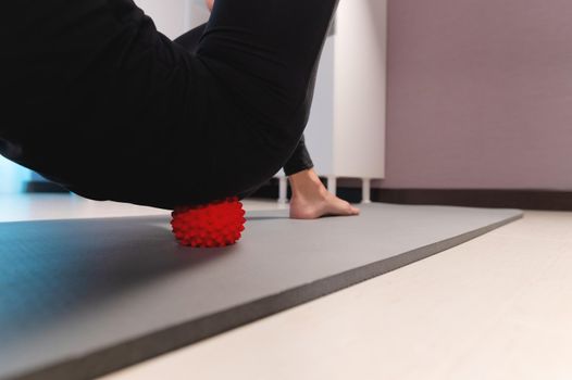 Close-up Athletic caucasian slim woman doing myofascial self-massage of the thigh and gluteus muscles in a massage room.