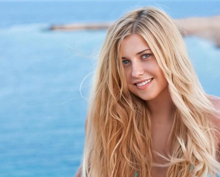 Beauty, wellness and summer portrait. Beautiful young woman with long blond hair, happy blonde smiling, blue sea on background.