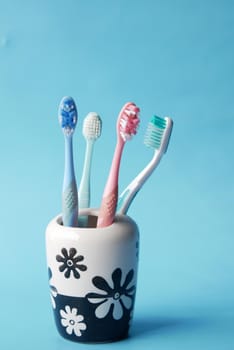 colorful toothbrushes in white mug against blue background .