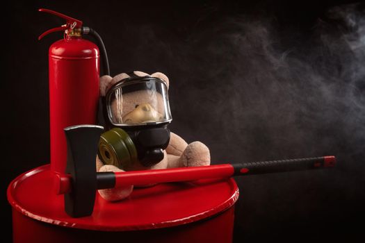 mascot of the fire brigade is a teddy bear in a gas mask with a fire extinguisher and a red axe in smoke on a dark background
