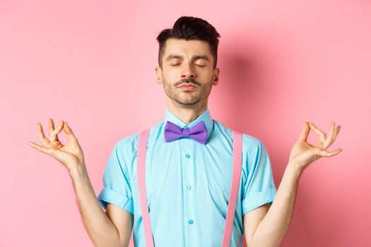 Young guy in bow-tie standing calm and peaceful, meditating with hands in mudra zen gesture and closed eyes, practice yoga to relax, standing over pink background.