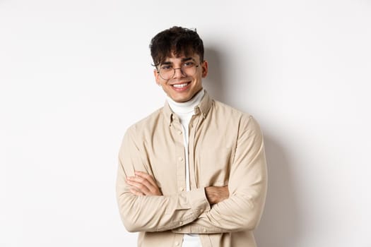 Handsome young man in glasses cross arms on chest, smiling at camera carefree, standing on white background.