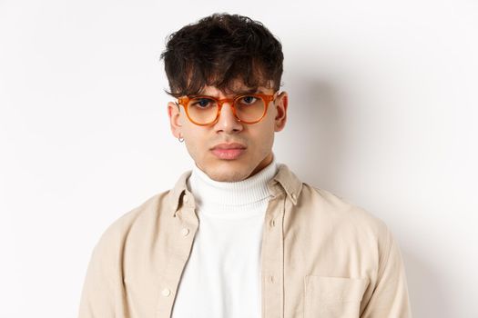 Close up portrait of angry frowning guy looking with dispise, standing mad on white background, wearing glasses.