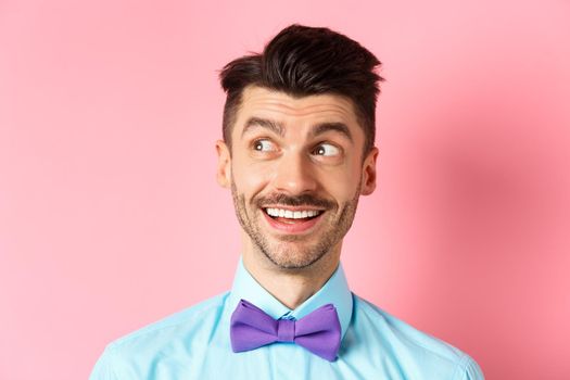 Close-up of amused smiling guy with moustache, pointing and looking left happy, stare at logo, standing on pink background. Copy space