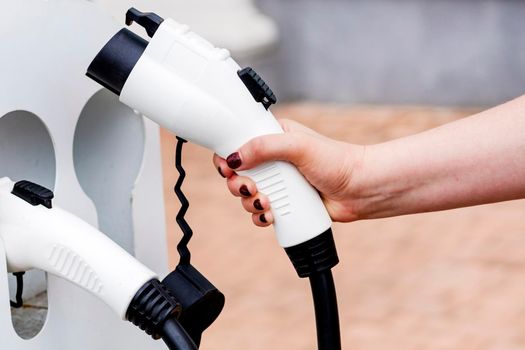 The female hand takes an electric vehicle charging cable. The driver picks up a cable to charge the electric vehicle. Eco-friendly alternative energy concept.close-up