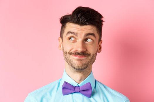Close-up of handsome smiling guy with moustache, looking left at logo with pleased face, standing on pink background. Copy space