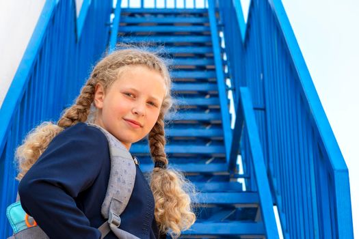 Schoolgirl with a smile climbs the stairs. Concept  school days, start date, next stage, career ladder, the beginning of the way. girl in a uniform with a backpack. Girl near the stairs.
