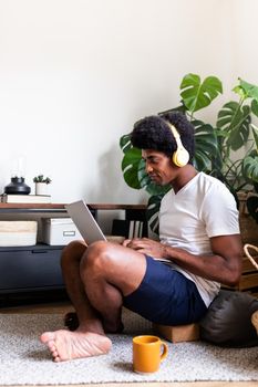 Young african american man typing in his laptop wearing headphones in cozy living room. Vertical image. Copy space. At home concept. Technology concept.