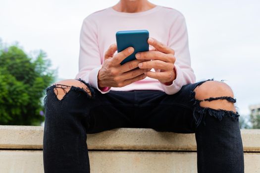 Unrecognisable caucasian man with pink sweater holding cellphone reading text messages. Using mobile phone apps. Social media concept.