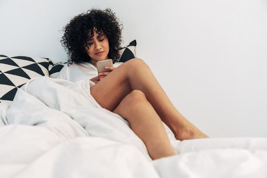 Young mixed race woman using mobile phone in bed. Copy space. Lifestyle and social media concept.