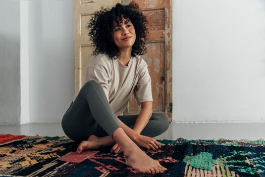 Pensive young multiracial smiling woman sitting on floor looking away. Copy space. Contemplation concept.
