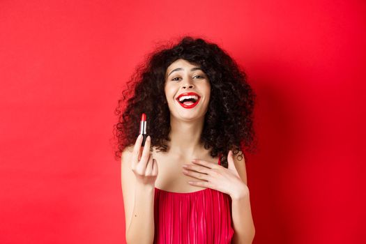 Elegant woman in dress, showing red lipstick and laughing, standing over studio background. Copy space