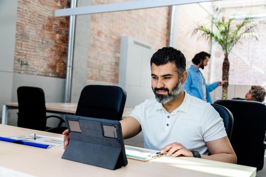 Happy Indian male entrepreneur working at the office using a digital tablet. Copy space. Startup concept.