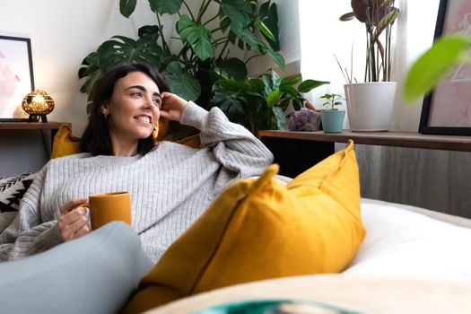 Happy young woman relaxing at home with tea looking out the window. Copy space. Lifestyle concept.