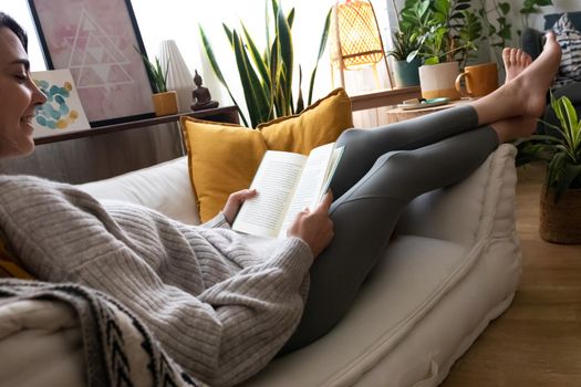 Happy young caucasian woman reading a book at home. Relaxing on the sofa. Lifestyle concept.
