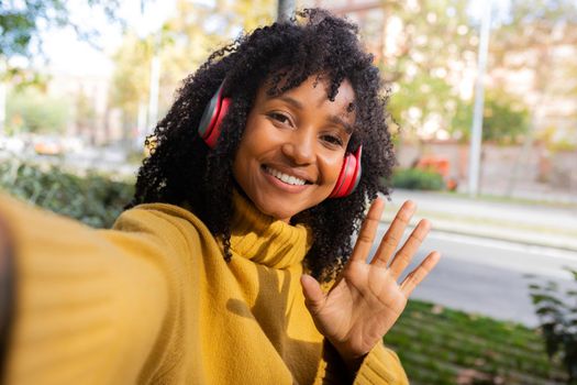 Young African American woman waving at camera takes selfie in city park. Lifestyle and social media concepts.