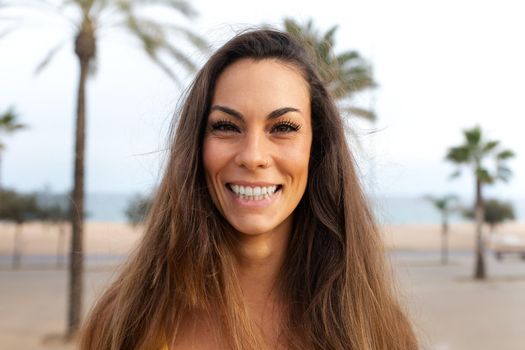 Headshot of smiling caucasian young woman looking at camera. Beach background with palm trees. Lifestyle concept.