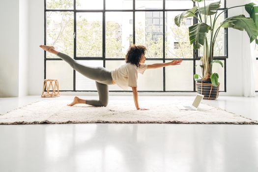 Young multiracial woman exercising at home with online fitness program using laptop. Copy space. Active and healthy lifestyle concept.