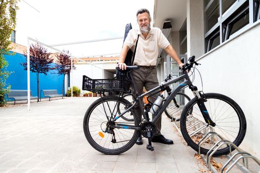 Mature caucasian man standing next to his bicycle in a bike parking space. Copy space. Urban traveling concept.