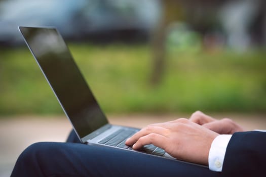 Man working on his laptop outdoors. Business man hands typing on computer. High quality photo
