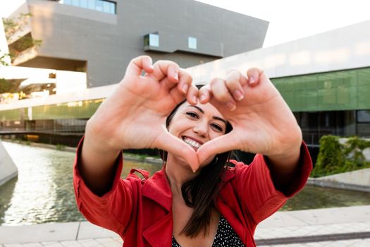 Young caucasian woman looking at camera makes heart shape with fingers. Showing love and affection concept.