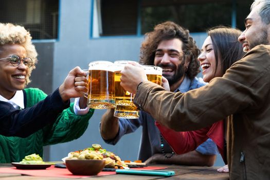 Happy young multiracial friends celebrate toasting with beer in an outdoors bar. Happiness and friendship concept.