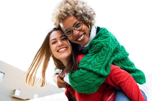 Playful smiling multiracial female lesbian couple looking at camera. African american woman piggyback ride with girlfriend. Copy space. LGBT concept.