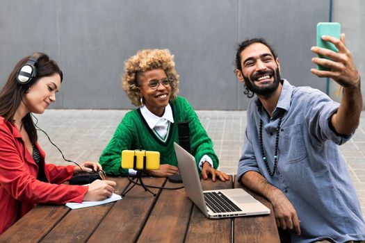 Young multiracial influencers take selfie with mobile phone while live streaming and recording podcast. Technology and social media concept.