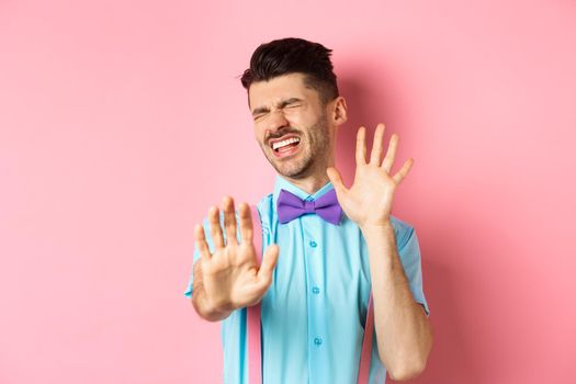 Crying guy asking to stop, raising hands up in defense, protecting himself from assault, standing over pink background.