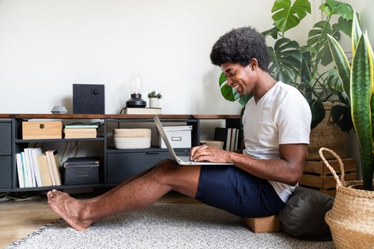 Happy and smiling young african american man typing on laptop in his cozy warm apartment. Copy space. At home concept. Technology.