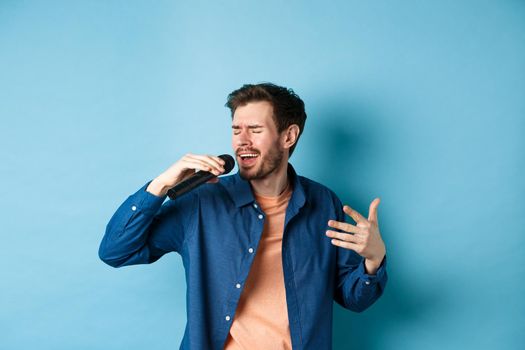 Romantic guy singing song in microphone and gesture, singer playing karaoke, standing on blue background.