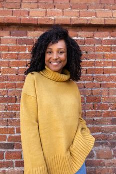 Vertical portrait of African American woman with curly hair wearing yellow sweater. Brick background wall. Lifestyle concept.