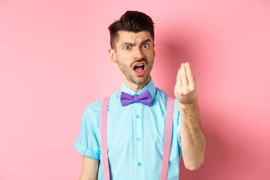 Impulsive young man having an arument, prove someone wrong, showing italian gesture and complaining, standing over pink background.